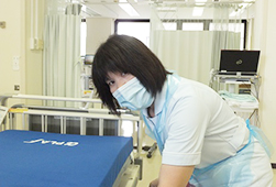 白い制服を着て水色のエプロンを付け作業をしている看護助手の女性の写真