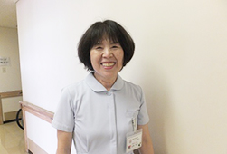 薄い水色の制服を着てカメラに笑顔を向ける看護助手の女性の写真