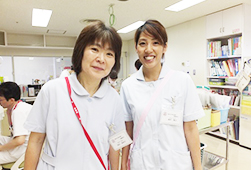 白い制服を着た看護助手の2人がナースステーションで笑顔で並んでいる写真