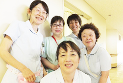 病院の廊下で、1人がかがんで前に立ち、その後ろに4人が並んで立つ笑顔の看護助手5人の写真