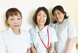 薄い水色の制服を着た看護助手の3人が笑顔で寄り添って並んでいる写真
