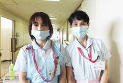 薄い水色の制服を着てマスクをつけている看護助手の2人が廊下で並んでいる写真