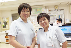 白い制服を着た看護助手の2人がパソコンの前で笑顔で並んでいる写真